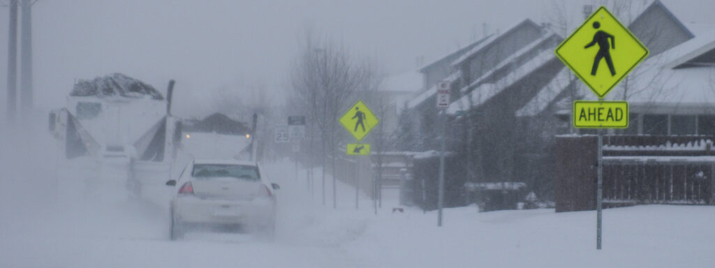 Snowplows clearing streets with pedestrian signs in the foreground